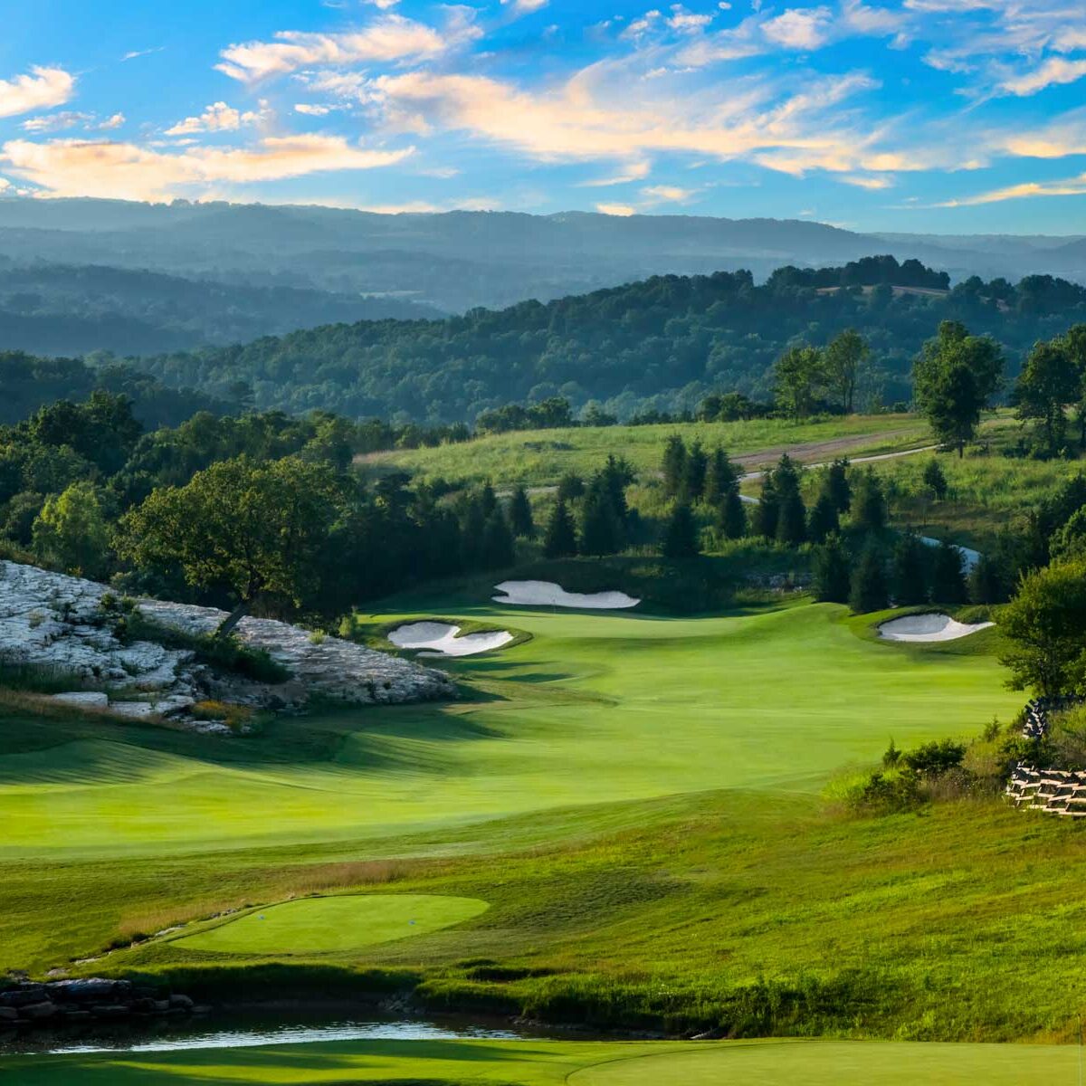 A view of a golf course with trees and mountains in the background.